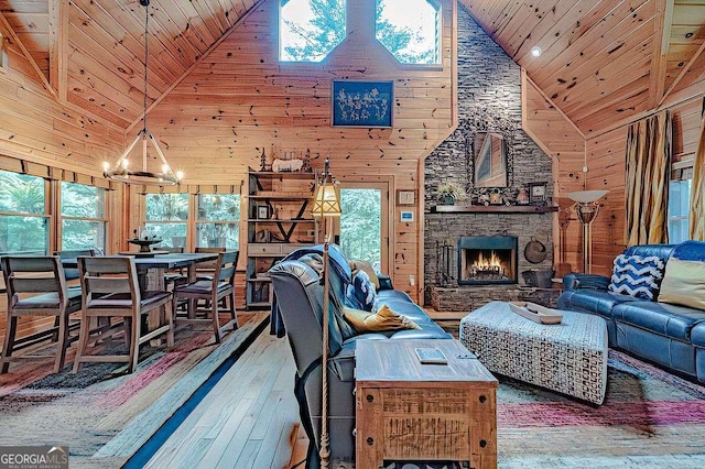 living area with a stone fireplace, wooden walls, wood ceiling, hardwood / wood-style floors, and an inviting chandelier