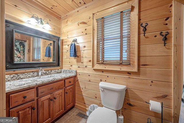 bathroom featuring toilet, vanity, wooden walls, and tile patterned flooring