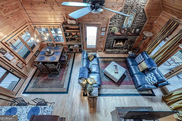 unfurnished living room with ceiling fan, a stone fireplace, hardwood / wood-style flooring, and wooden walls