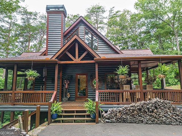 view of front facade with a porch, faux log siding, a shingled roof, and a chimney