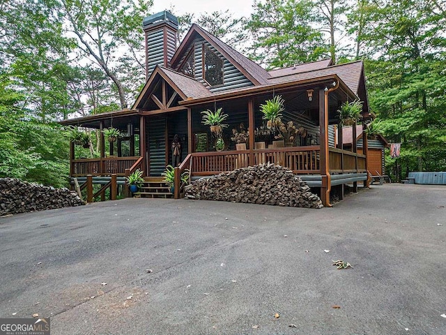 view of front of house with a shingled roof, a chimney, and a porch