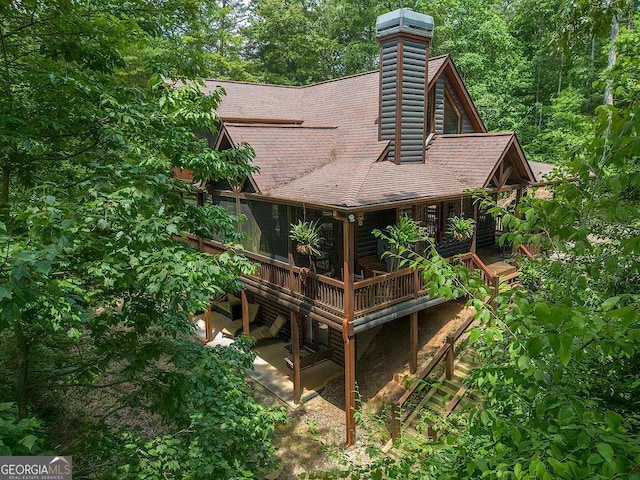 exterior space with gutters, a shingled roof, a chimney, and a downspout