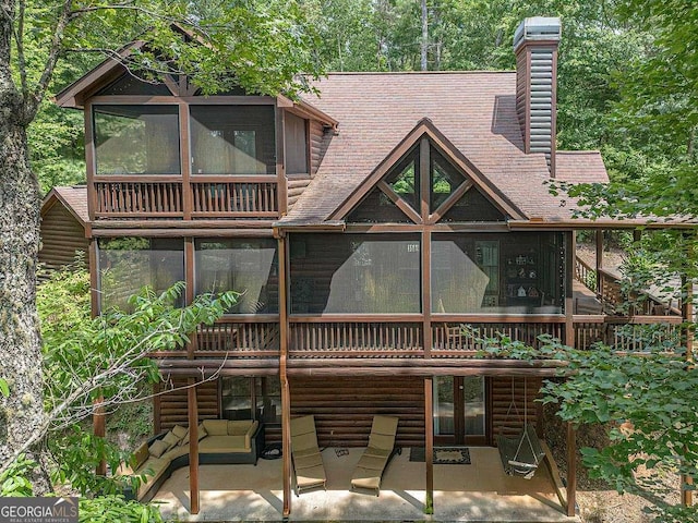 back of property featuring a chimney, a wooden deck, a sunroom, and faux log siding