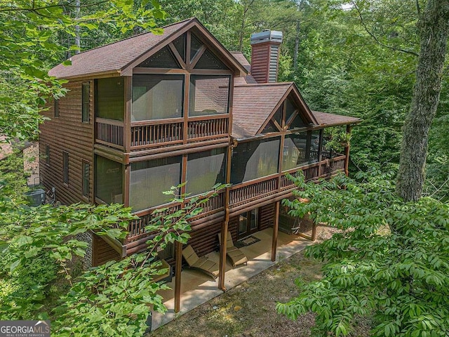 rear view of house featuring a sunroom, a patio area, a chimney, and roof with shingles