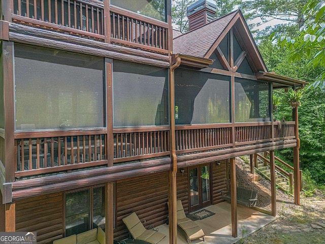 view of side of property with faux log siding, a sunroom, roof with shingles, and a chimney