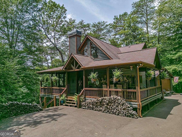 chalet / cabin with covered porch, roof with shingles, and log veneer siding