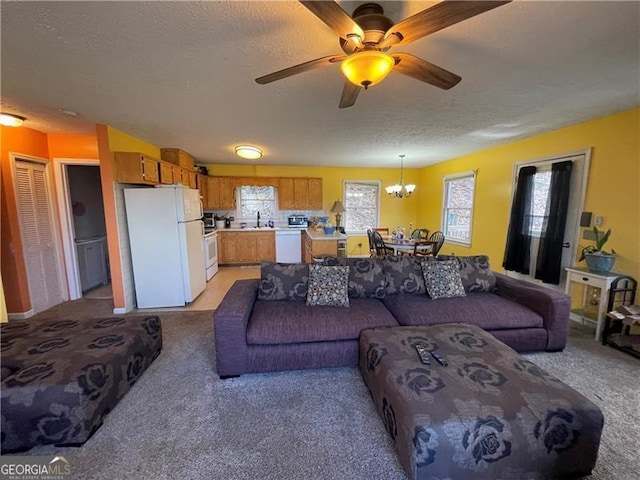 carpeted living room with sink, ceiling fan with notable chandelier, and a textured ceiling