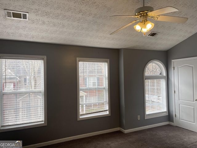 empty room featuring ceiling fan, lofted ceiling, dark carpet, and a textured ceiling