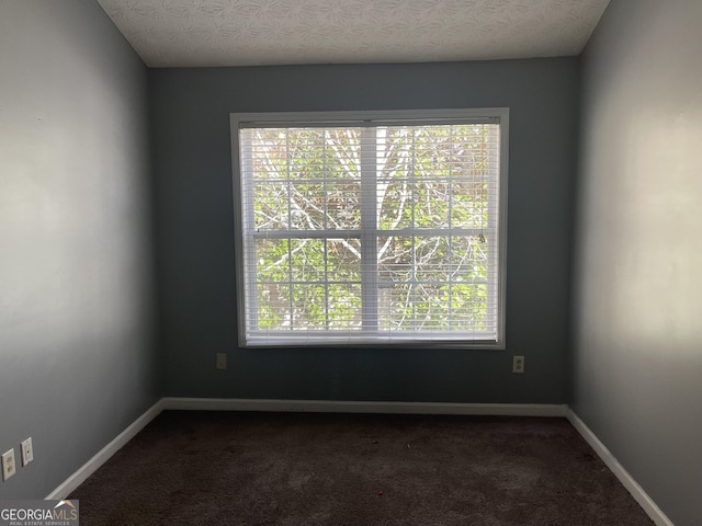 empty room with a textured ceiling, a healthy amount of sunlight, and dark colored carpet