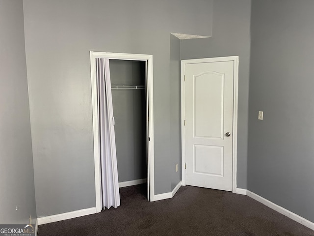 unfurnished bedroom with dark carpet and a closet