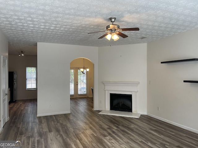 unfurnished living room featuring dark wood-type flooring, plenty of natural light, ceiling fan with notable chandelier, and a textured ceiling