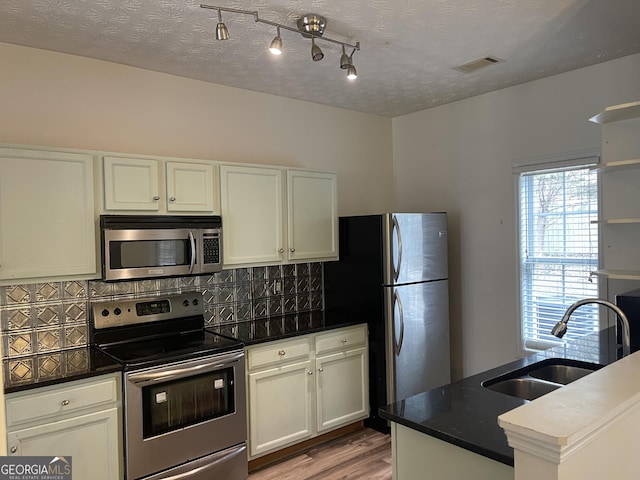 kitchen with sink, light hardwood / wood-style flooring, appliances with stainless steel finishes, backsplash, and white cabinets