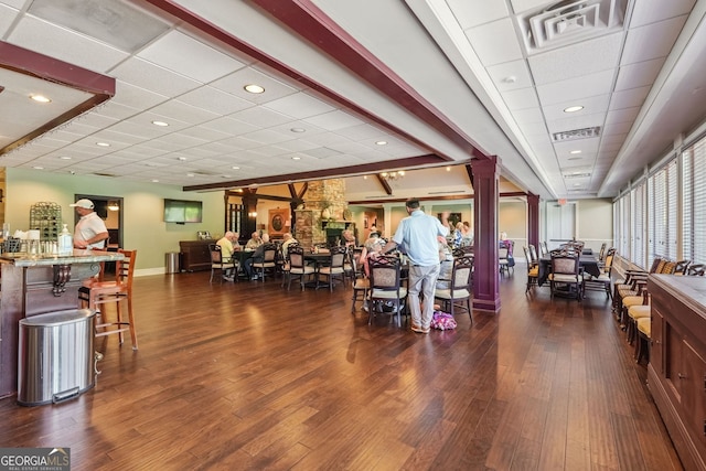 exercise room with dark wood-type flooring, indoor bar, a drop ceiling, and ornate columns