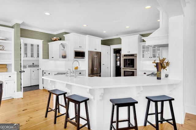 kitchen featuring stainless steel appliances, washing machine and dryer, white cabinets, and light hardwood / wood-style floors