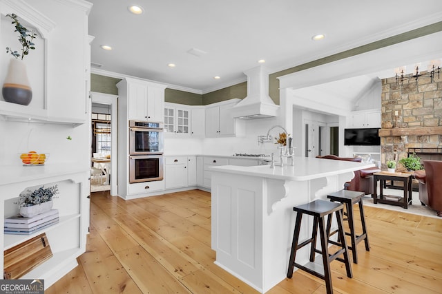 kitchen with a breakfast bar, white cabinets, custom exhaust hood, kitchen peninsula, and stainless steel double oven