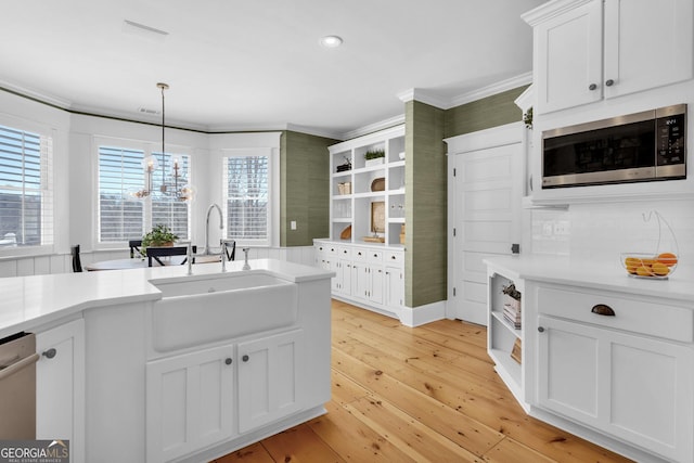 kitchen featuring sink, crown molding, stainless steel appliances, white cabinets, and decorative light fixtures