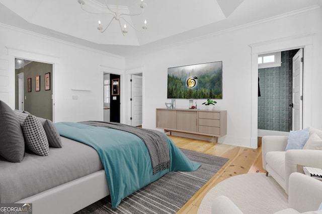 bedroom featuring hardwood / wood-style flooring, crown molding, ensuite bathroom, a tray ceiling, and a chandelier