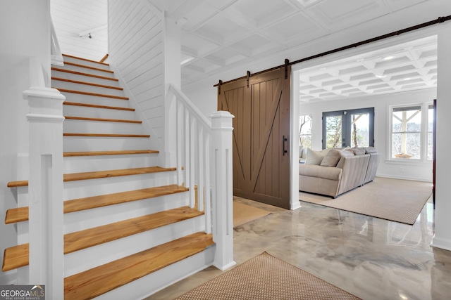 staircase featuring coffered ceiling, a barn door, and concrete flooring