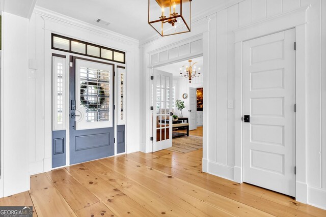 entryway featuring hardwood / wood-style flooring, ornamental molding, and a notable chandelier