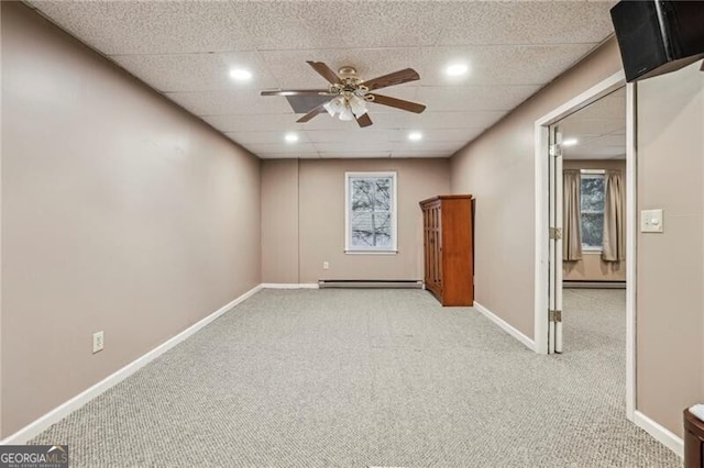 empty room featuring light carpet, baseboard heating, ceiling fan, and a drop ceiling