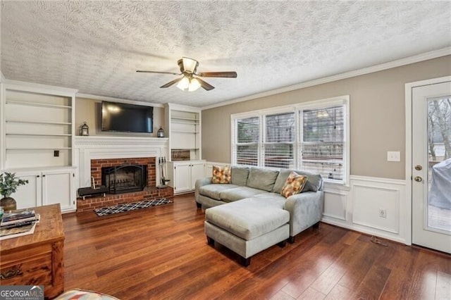 living room featuring built in features, ornamental molding, a textured ceiling, dark hardwood / wood-style flooring, and a brick fireplace