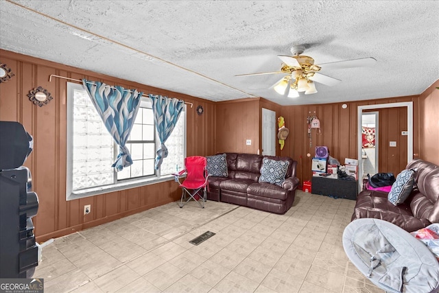 living room featuring ceiling fan, a textured ceiling, and wood walls