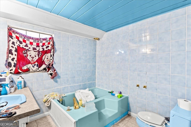 bathroom featuring tile patterned floors, a tub to relax in, toilet, tile walls, and vanity