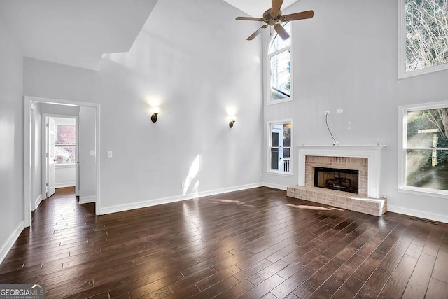 unfurnished living room with ceiling fan, a towering ceiling, a fireplace, and dark hardwood / wood-style flooring