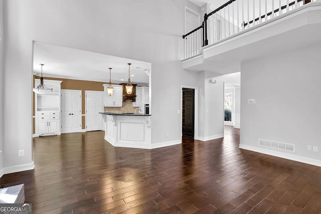 unfurnished living room with dark wood-type flooring, sink, and a towering ceiling