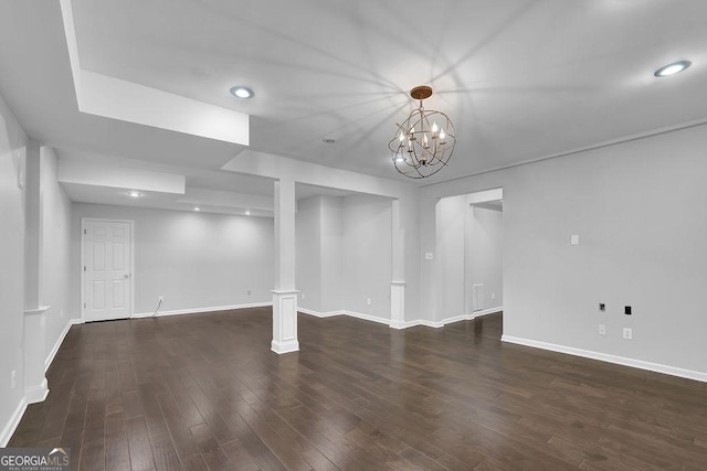 empty room with dark hardwood / wood-style floors, decorative columns, and a notable chandelier