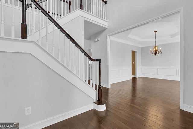 entryway with an inviting chandelier, a tray ceiling, dark wood-type flooring, and crown molding