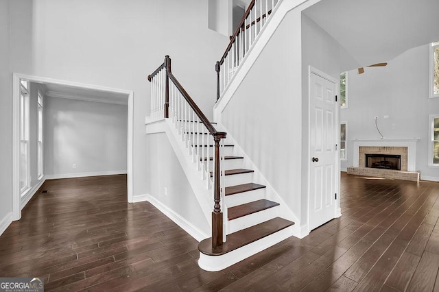 stairway featuring a high ceiling, wood-type flooring, a brick fireplace, and a healthy amount of sunlight