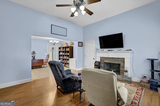 living area featuring baseboards, wood finished floors, and a stone fireplace