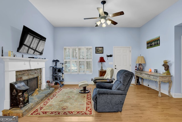 living area featuring a ceiling fan, a brick fireplace, baseboards, and wood finished floors