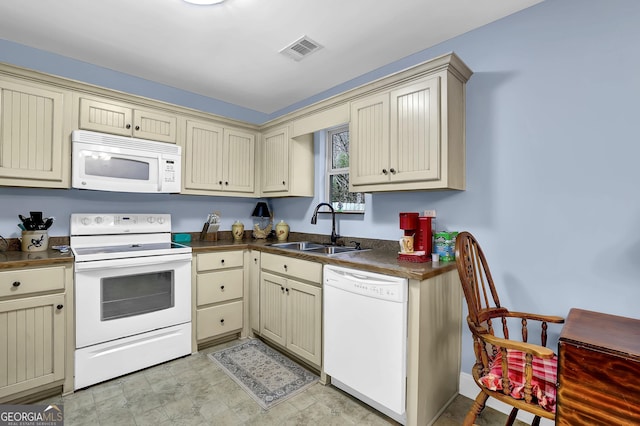 kitchen featuring dark countertops, visible vents, cream cabinets, a sink, and white appliances