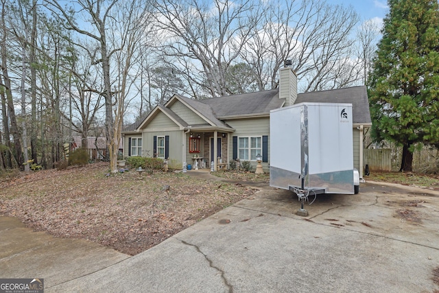 view of front of house with a shingled roof, concrete driveway, fence, and a chimney