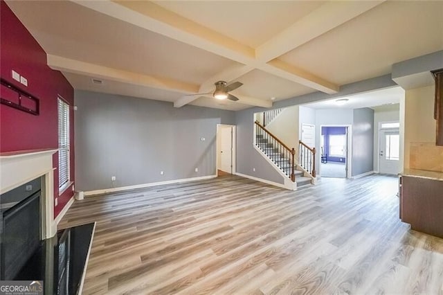 unfurnished living room with coffered ceiling, ceiling fan, light hardwood / wood-style flooring, and beamed ceiling