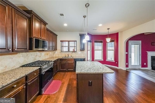 kitchen with hanging light fixtures, stainless steel appliances, light stone countertops, a kitchen island, and dark hardwood / wood-style flooring