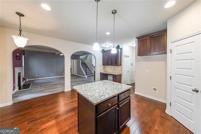 kitchen featuring dark wood-type flooring, hanging light fixtures, dark brown cabinets, light stone countertops, and a kitchen island