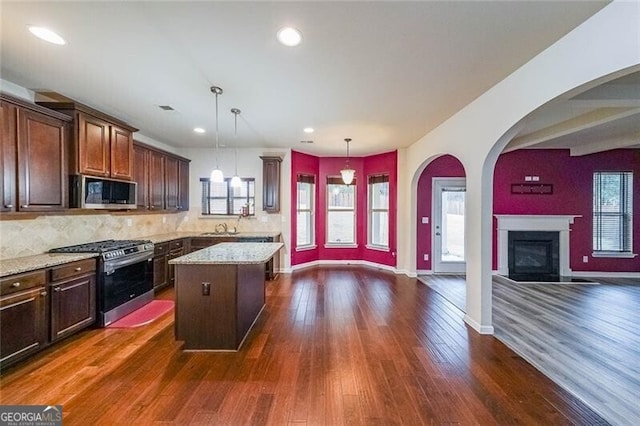 kitchen with appliances with stainless steel finishes, dark hardwood / wood-style floors, pendant lighting, a center island, and light stone counters