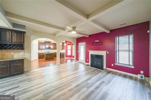 unfurnished living room featuring ceiling fan, light hardwood / wood-style floors, a premium fireplace, and beamed ceiling