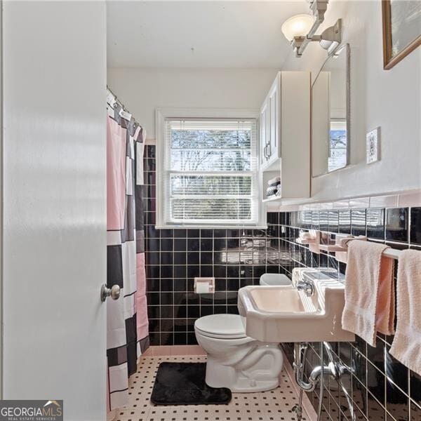 bathroom with tile patterned floors, toilet, sink, and tile walls