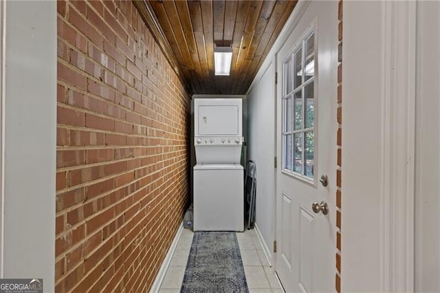 laundry room featuring light tile patterned floors, wooden ceiling, brick wall, and stacked washer / dryer