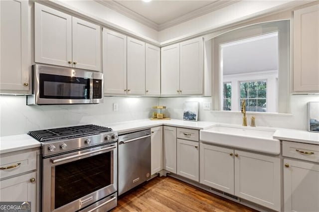 kitchen featuring appliances with stainless steel finishes, sink, decorative backsplash, hardwood / wood-style flooring, and crown molding