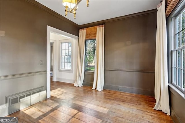 spare room featuring crown molding, plenty of natural light, a chandelier, and wood-type flooring