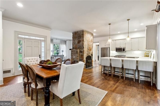 dining room featuring crown molding, a stone fireplace, and hardwood / wood-style floors