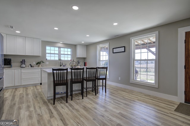 kitchen with light countertops, a breakfast bar, white cabinetry, and baseboards