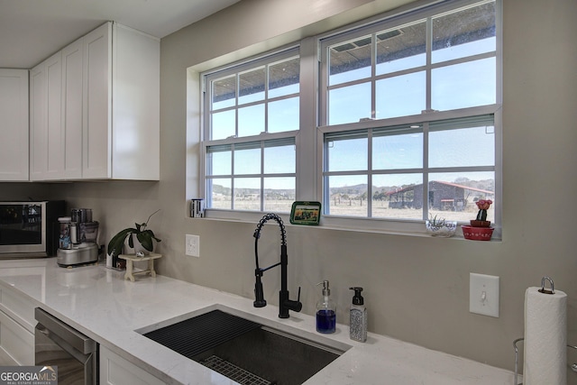 kitchen featuring light stone countertops, white cabinetry, and a sink