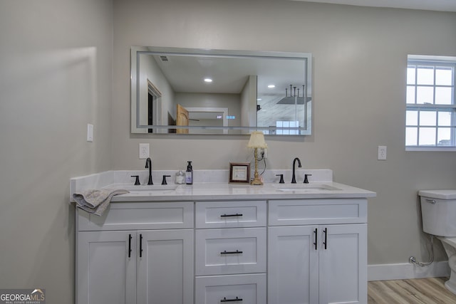 full bath with toilet, wood finished floors, a sink, baseboards, and double vanity