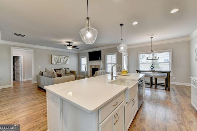 kitchen with light hardwood / wood-style flooring, a kitchen island with sink, hanging light fixtures, and white cabinets